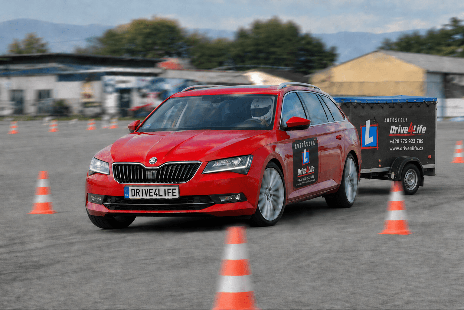 A red Škoda Superb driving at high speed through a slalom of orange cones with a trailer attached.